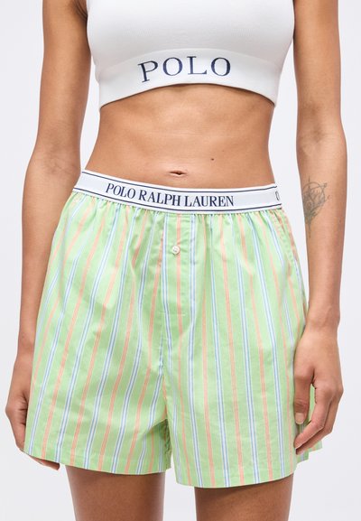 Γυναίκα που φοράει πράσινο ριγέ σορτς Polo Ralph Lauren και λευκό κροπ τοπ με το κείμενο "POLO", αποκαλύπτοντας το μέσο του σώματος και ένα τατουάζ στον πήχη.