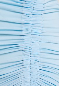 Vaaleansininen kapea mekko, jossa on pystyröyhelöinti edessä. Se on valmistettu sileästä kankaasta, jossa on hieman joustava tekstuuri.