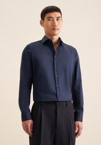 Navyblauw overhemd met lange mouwen, knoopsluiting aan de voorkant en een slim-fit pasvorm. Glad materiaal met een subtiele glans en contrasterende details in de binnenste kraag.