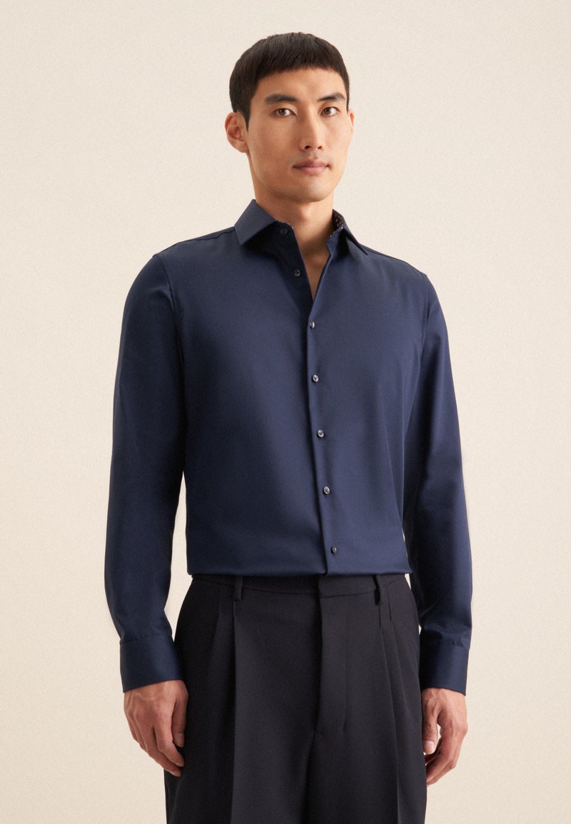 Navyblauw overhemd met lange mouwen, knoopsluiting aan de voorkant en een slim-fit pasvorm. Glad materiaal met een subtiele glans en contrasterende details in de binnenste kraag.