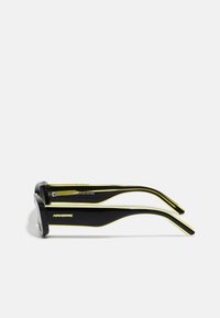 Black and yellow bio-acetate sunglasses with a thick frame, featuring a sleek design, bold color contrast, and subtle branding on the temple.