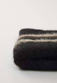 Schwarz- und braun gestreifte Wolldecke, gefaltet. Weiche Textur mit einem fusseligen Aussehen, mit horizontalen Streifen in Beige und Braun.