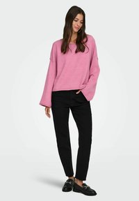 Różowy, oversize sweter z szerokimi rękawami, w połączeniu z czarnymi, tapered dżinsami i czarnymi loafersami. Zauważony prosty design i miękka struktura.