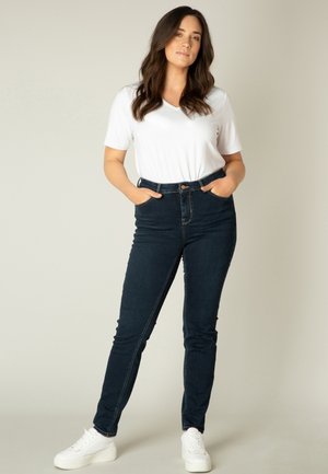 Donkerblauwe high-waisted jeans met een slim fit, gecombineerd met een wit T-shirt met korte mouwen en een V-hals, en witte sneakers.