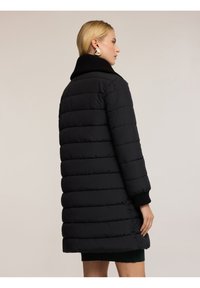 Zwarte pufferjas met hoge kraag, voorzien van horizontale stiksels, gebreide manchetten en een middellange snit. Glad textuur met een elegante uitstraling.