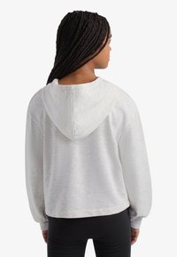 Svetlo siva obrezana jopa s strukturirano površino, kapuco z zategovalno vrvico in rahlo napihnjenimi rokavi; kombinirana s črnimi pajkicami.