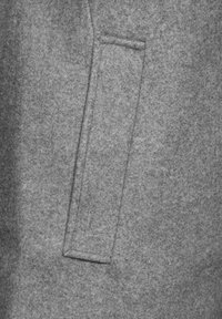 Grå filtmaterial med en slät textur, utrustad med en rektangulär fackficka som visar en noggrann söm utan synlig sömnad.