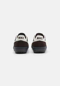 Crne nubuk tenisice s bijelim kožnim ovratnikom, s "NIKE" logom na peti, pojačanom gumenom potplatom i teksturiranim detaljima.