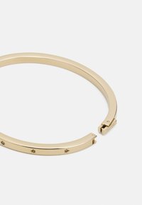 Armband aus goldfarbenem Metall mit einem eleganten, geschwungenen Design, das kleine Sternelemente und einen klappbaren Verschluss aufweist. Glatte, glänzende Oberfläche.