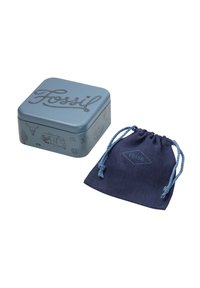 Boîte métallique bleue de marque Fossil avec des motifs vintage à côté d'une pochette à cordon bleu marine avec le logo Fossil.