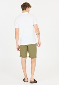 Witte polo, olijfgroene shorts en bruine sliders. Gefocust op de achterkant, laat casual zomeroutfit en een tattoo zien.