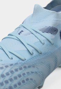 Scarpetta da calcio azzurro chiaro con tomaia in maglia testurizzata, dettagli grafici blu e lacci abbinati annodati sul davanti.