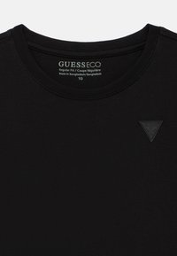 Μαύρο T-shirt με στρογγυλή λαιμόκοψη, με την ετικέτα GUESS ECO τυπωμένη εσωτερικά στο γιακά και μαύρο τρίγωνο με το λογότυπο GUESS στο στήθος.