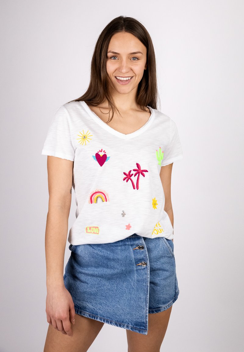 White V-neck t-shirt featuring colorful embroidered patches including hearts, palm trees, and a rainbow, paired with a denim A-line skirt.