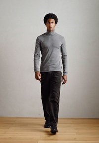 Szürke garbó, slim fit szabású, sötét kordbársony nadrággal viselve. Sima tapintás és egyszerű dizájn, fekete cipővel párosítva. Világos fa padló.