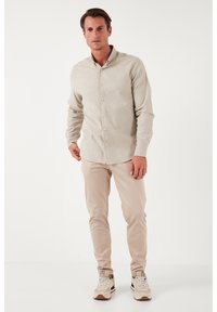 Camicia button-up beige chiaro, slim fit, in tessuto testurizzato. Abbinata a pantaloni beige chiaro e sneakers con dettagli in crema e marrone.