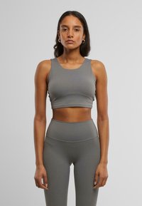 Sivi crop top s širokim trakama i bešavnim dizajnom, uparen s rastezljivim sivoj tajicama visoki struk. Glatka tkanina s pripijenom siluetom.