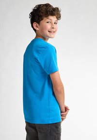 Camiseta de algodón de color azul brillante, con mangas cortas, cuello redondo y un ajuste relajado. La vista trasera muestra una textura suave y un diseño sencillo.
