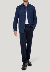 Blaues Denim-Hemd mit Knöpfen und zwei Brusttaschen, getragen über einem weißen T-Shirt. Kombiniert mit marineblauen Hosen und schwarzen Lederschuhen.