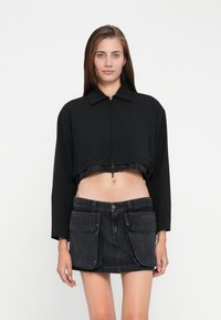 Zwarte cropped jas met een kraag en ritssluiting, gecombineerd met een donkere denim rok met opgestikte zakken.