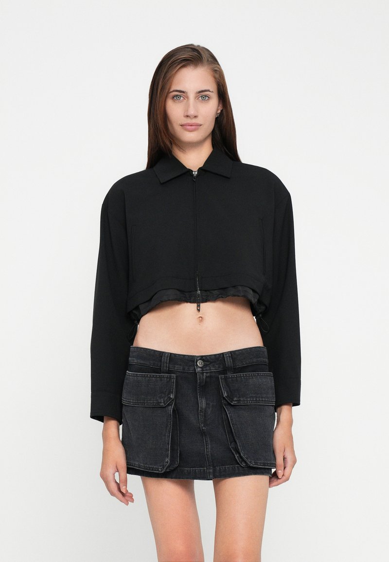 Zwarte cropped jas met een kraag en ritssluiting, gecombineerd met een donkere denim rok met opgestikte zakken.