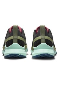 Chaussures de sport noires avec des accents verts et une doublure rose, dotées d'une surface texturée, d'une semelle rembourrée et d'une bride au talon pour un enfilage facile.