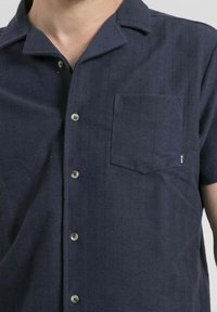 Chemise à manches courtes bleue marine en tissu texturé. Dotée d'un devant à boutons, d'un col et d'une poche poitrine. Motif à fines rayures verticales.