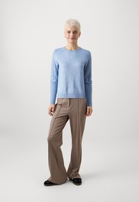 Maglione lavorato a maglia di colore azzurro chiaro con scollatura rotonda e bordo a coste, abbinato a pantaloni larghi beige, su uno sfondo bianco semplice.