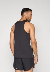 Camiseta deportiva negra sin mangas con escote redondo y franjas blancas laterales; fabricada con tela ligera y transpirable.