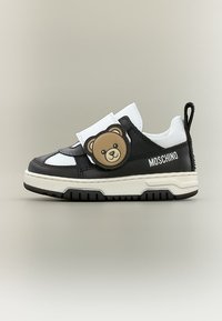 Ασπρόμαυρο sneaker Moschino με πρόσωπο αρκουδάκι στη λουρίδα και χοντρή λευκή σόλα, πλευρική όψη σε απλό φόντο.