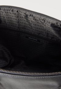 Εσωτερικό μαύρης δερμάτινης τσάντας με ορατή τσέπη με φερμουάρ και επαναλαμβανόμενο κείμενο "ARMANI EXCHANGE" στη φόδρα μέσα στην τσάντα.