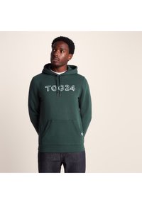 Green hooded sweatshirt made of cotton blend, featuring a large white "TOG24" logo, kangaroo pocket, and ribbed cuffs and hem.