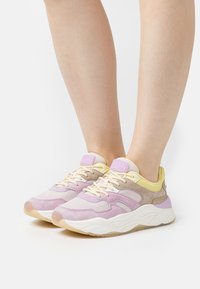 Sport sneakers in predominantly light purple and yellow with mesh and suede materials. Features a thick white sole and contrasting accents.