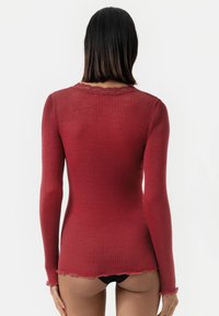 Rode geribbelde longsleeve top met een scalloped halslijn en zoom. Stof lijkt zacht, met een getailleerd ontwerp dat de lichaamshouding benadrukt.