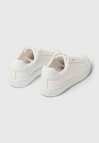 Bijele tenisice s glatkom kožnom gornjom stranom, okruglim vrhom i podstavljenim ovratnikom. Imaju teksturiranu gumenju potplat i minimalistički dizajn.