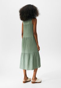 Robe maxi en coton vert avec un design texturé et à volants. Dotée de bretelles réglables et d'une silhouette fluide. Associée à des sabots légers.