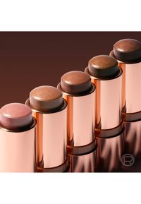Five shimmering makeup sticks in rose gold tubes, arranged diagonally with colors from light pink to deep brown.