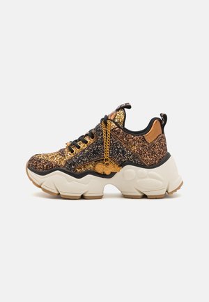 Glitzernde schwarze und goldene Sneaker mit einer klobigen weißen Sohle. Merkmale sind das schnürbare Design, eine goldene Kettenakzentuierung und ein strukturiertes Obermaterial.