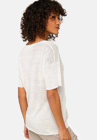 Lightweight, off-white knit t-shirt with short sleeves, relaxed fit, and a soft texture, featuring a rounded neckline and back seam detail.