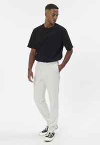 Schwarzes T-Shirt mit kurzen Ärmeln, hellgraue, maßgeschneiderte Hose und schwarze Sneakers mit weißen Akzenten. Glatter Stoff mit lockerem Schnitt.