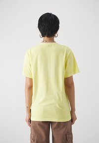 Camiseta de algodón de color amarillo claro con mangas cortas y cuello redondo, presenta una textura suave y un corte relajado en la parte posterior.