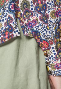 Multikleurige bloemenblouse van lichtgewicht stof met klokmouwen, gecombineerd met een textuurrijke olijfgroene rok met knoopaccenten.