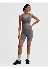 Grijze sportieve crop top en hoge taille shorts, gemaakt van rekbaar materiaal. Voorzien van een logo detail en een getailleerd ontwerp. Zwarte schoenen en witte sokken.