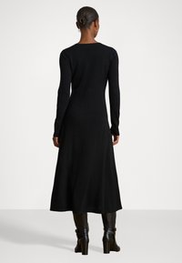 Vestido negro de manga larga con un cuerpo ajustado y falda acampanada, hecho de un tejido suave y texturizado. La parte trasera tiene un escote sutil en forma de scoop.