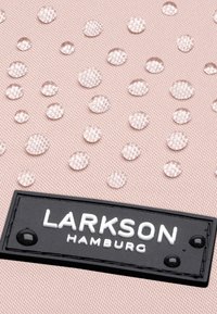 Rózsaszín, texturált anyag, egyértelmű cseppekkel és egy fekete címkével, amelyen fehér szöveg olvasható: "LARKSON HAMBURG." A cseppekből kör alakú minták láthatók.