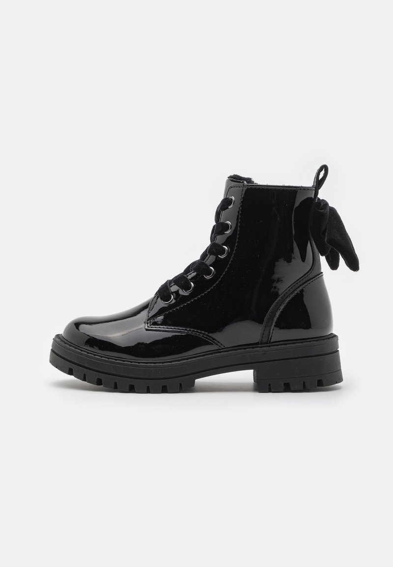 Bottine en cuir verni noir brillant avec semelle épaisse, lacets noirs et un nœud noir décoratif à l'arrière.