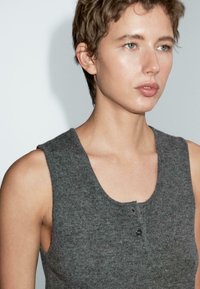 Top grigio senza maniche realizzato in morbido tessuto a maglia, con un collo rotondo e dettagli con bottoni sul davanti. Texture liscia e forma aderente.
