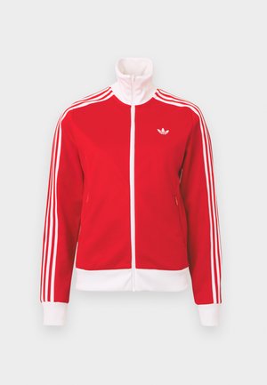 Červená sportovní bunda na zip s bílým zipem, třemi bílými pruhy na rukávech, bílými manžetami a lemem a bílým logem Adidas na hrudi.