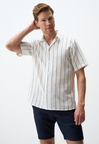 Korte mouwen shirt van witte linnen met marineblauwe verticale strepen, met een knoopsluiting aan de voorkant en een casual kraag. Gestyled met marineblauwe shorts.