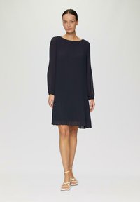Námořnické plisované šaty s dlouhými rukávy, kulatým výstřihem a splývavým střihem. Stylizované s lehkými sandály na pásky. Minimalistický design.